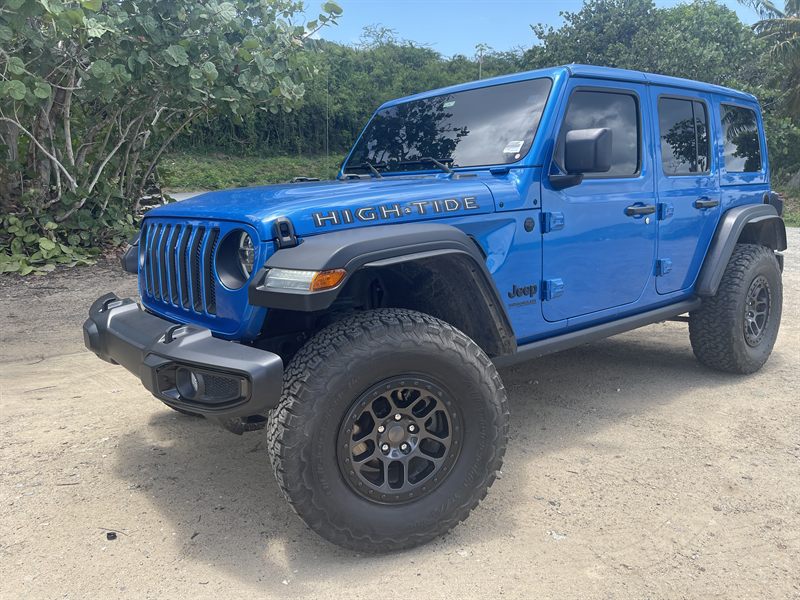 Blue Jeep Wrangler Unlimited High Tide on all-terrain tires and black alloy wheels, parked on a dirt track