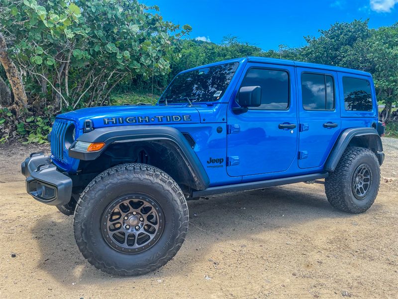 Blue Jeep Wrangler High Tide on a sandy track, with sea grape and palms behind