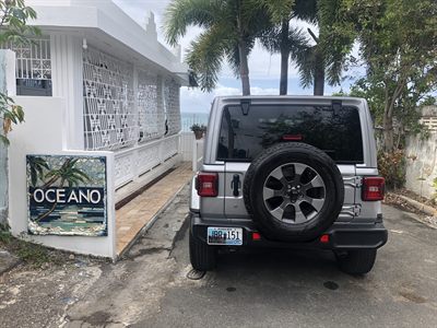 Rear of the silver Sahara with its tailgate-mounted spare, parked beside the Oceano mosaic sign