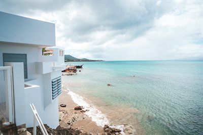 The white walls of the house dropping to the shoreline, with turquoise water and a moored boat beyond