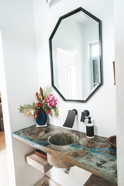 Powder room with an octagonal black-framed mirror above a poured stone basin and fresh flowers