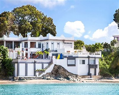 Oceano seen from the sea: a white multi-level house on the rocks above a small beach, framed by trees