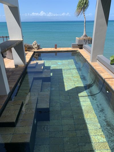 The cocktail pool from above, stone tiles under clear water and a carved stone head at the far end