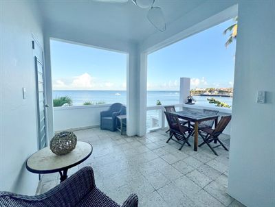 Covered terrace with wicker armchairs, a teak dining table and open views across the water to the harbor