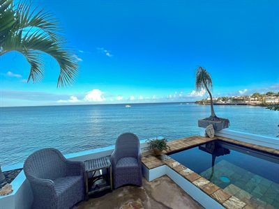 Wicker armchairs beside the cocktail pool, with the ocean and a palm filling the view
