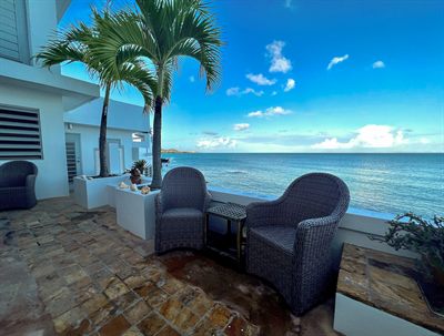 Two wicker armchairs on the stone terrace facing open water and a leaning palm
