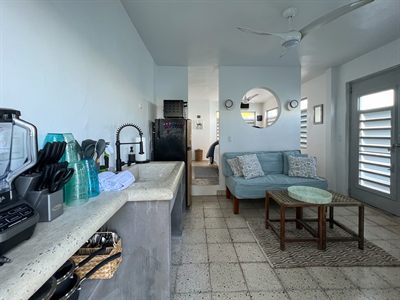 Open-plan kitchen and living area with a concrete counter, blue sofa and round mirror