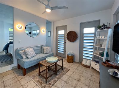 Living area with a blue sofa, round mirror, wall sconces, ladder shelf and television