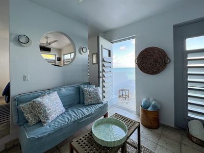 Sitting room with a blue sofa, round mirror and an open door onto the sea-facing terrace