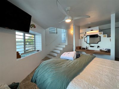 Bedroom with a wall-mounted television, a staircase rising behind the bed and a teal throw