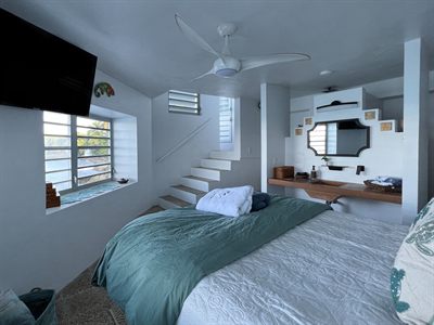 Bedroom with teal bedding, a staircase behind and a vanity with a black-framed mirror