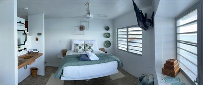 Wide view of the queen bedroom, teal throw and timber vanity beneath a round mirror
