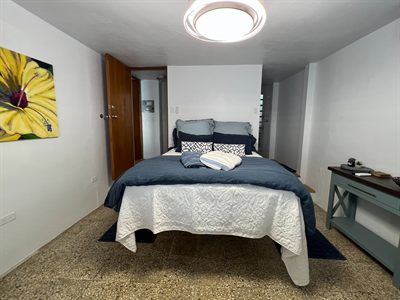 Bedroom with navy and white bedding, a timber wardrobe and a large yellow hibiscus painting