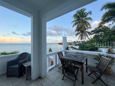 Teak table for four on the covered terrace at dusk, the sea flat and pale behind it