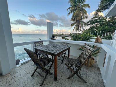 Teak dining table for four on a private balcony at sunset, with the sea and a palm behind