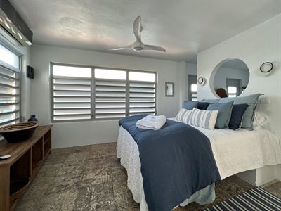 Bedroom with navy bedding, louvered windows and a timber console holding a carved bowl