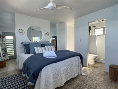 Bedroom with navy bedding beneath a round mirror, with the ensuite door open on the right