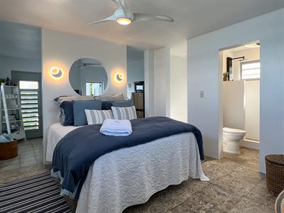 Bedroom with navy bedding, wall sconces either side of a round mirror, and an ensuite