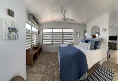 Bedroom with a queen bed in navy linen, louvered windows and a round mirror