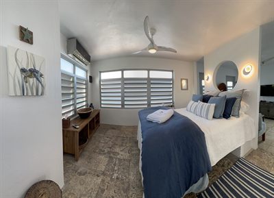 Bedroom with blue bedding, a louvered bay window and botanical artwork on the wall
