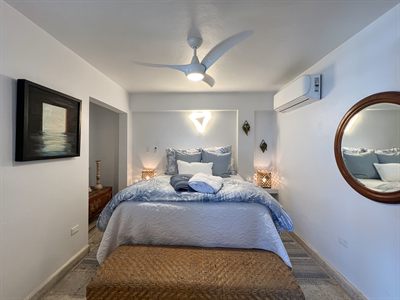 Bedroom with pale blue bedding, a framed seascape and a round timber mirror