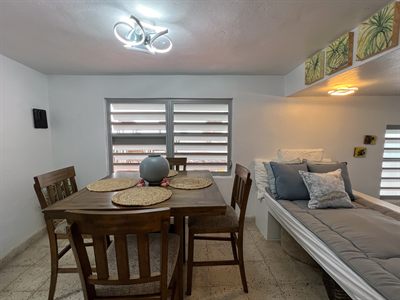 Dining table for four beside a built-in daybed piled with cushions, under framed pineapple prints