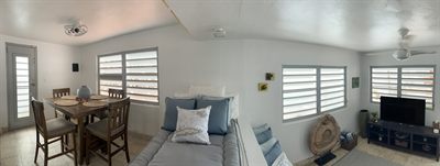 Open living area with a dining table, sofa and television, lit by louvered windows on three sides