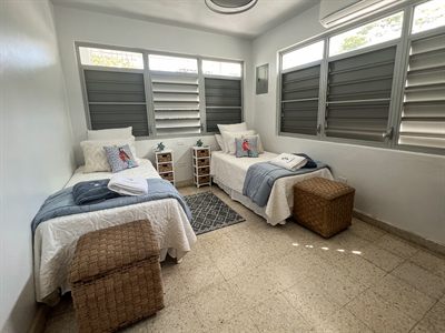 Twin bedroom with two single beds, woven storage trunks and louvered windows on two walls