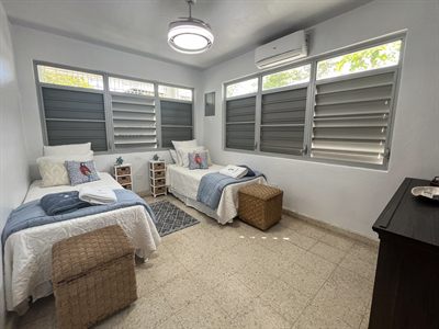 Twin room with two single beds, woven trunks and louvered windows on three sides