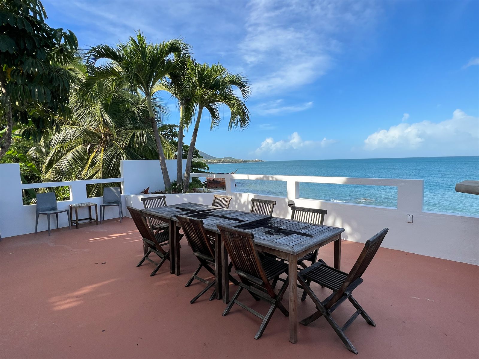 The upper terrace at Oceano, a long teak table set for eight with palms and open ocean beyond
