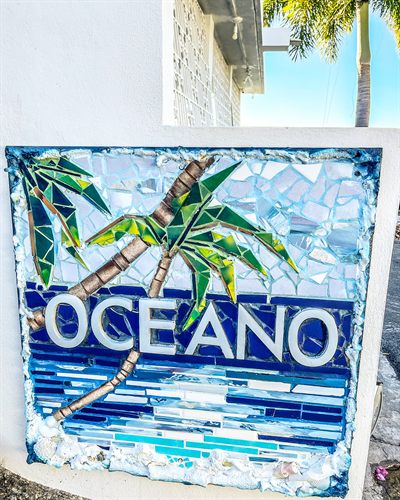 Hand-made glass mosaic sign reading Oceano, with palm trees above bands of blue tile