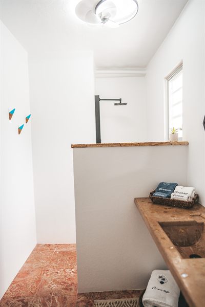 Outdoor shower with a timber ledge, terracotta floor and Oceano-embroidered towels