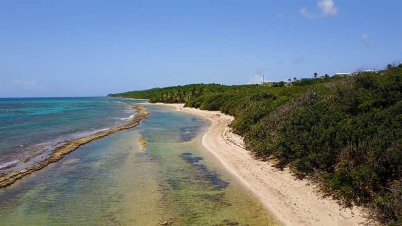 Aerial view along a mile of empty beach with reef in clear green water