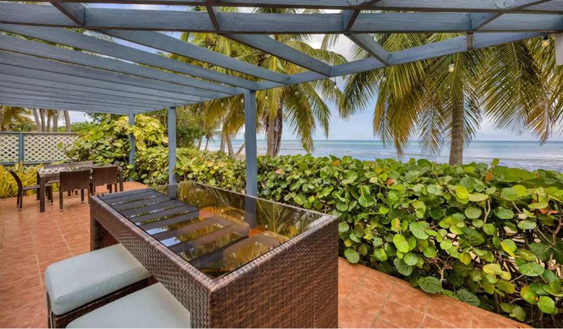 Beachfront pergola at Paradise Cove Suites with a shaded bar and palms framing the sea
