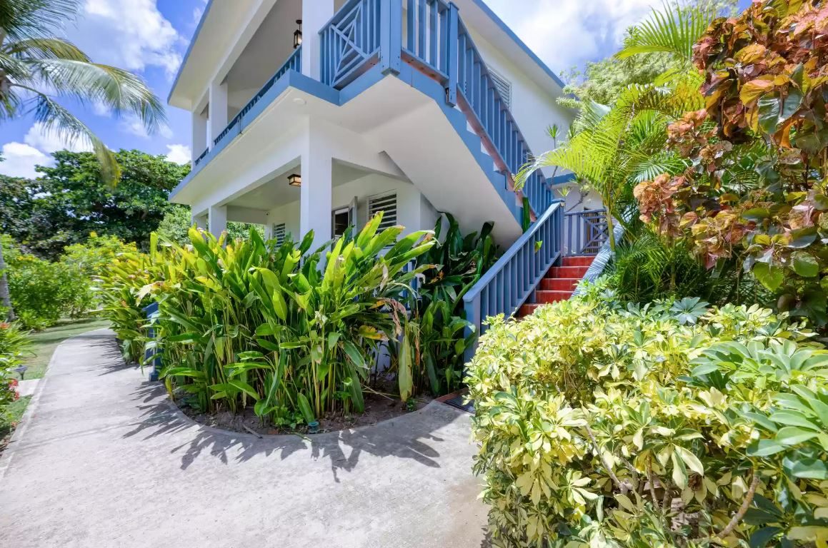 Paradise Cove Suites: a two-story blue and white house behind heliconia, an outside staircase climbing to the upper casita