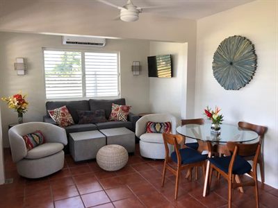 Open living and dining area with a gray sofa, swivel chairs, a round glass table and terracotta tile