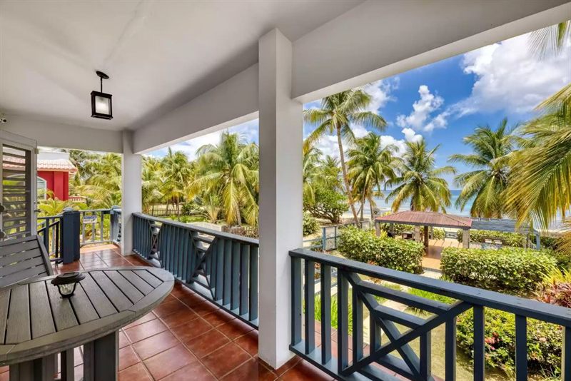 Media Luna's upstairs balcony, blue railings and a timber table, looking over the palms to the gazebo and the sea