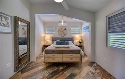 Media Luna bedroom with a king bed, twin lamps, a leaning mirror and reclaimed-look plank flooring