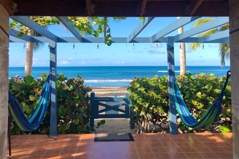 Covered patio with two hammocks looking through a garden gate to the Caribbean