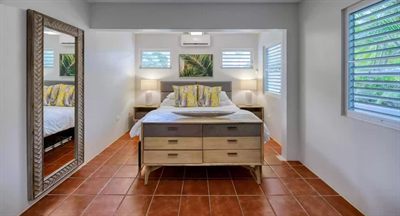 Sun Bay bedroom with a king bed between matching lamps, a tall leaning mirror, louvered windows and terracotta tile