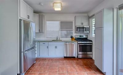 Sun Bay kitchen with white cabinetry, a stainless gas range, dishwasher and fridge, and a terracotta tiled floor