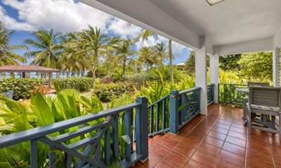 Sun Bay's covered lanai with blue timber railings and terracotta tile, looking over tropical planting to the sea