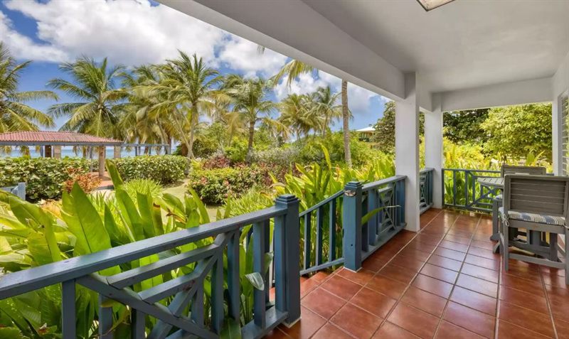 Sun Bay's covered lanai, blue timber railings and terracotta tile, looking over tropical planting to the sea
